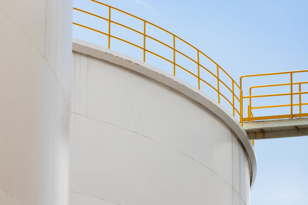 化工厂的白色钢制水箱，配有黄色扶手。工厂里的大金属筒仓，蓝天背景。图片下载