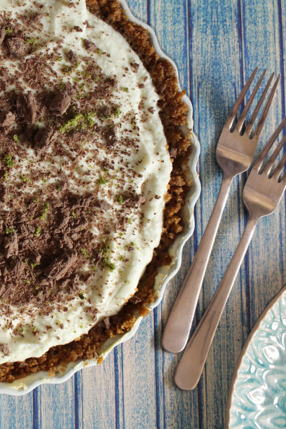 柠檬柠檬芝士蛋糕和黄油姜饼干的图片，以蓝色的舌和凹槽效果为背景，旁边有两把叉子和一个盘子，柑橘马斯卡邦奶油奶酪甜点布丁，上面有磨碎的牛奶巧克力，酸橙皮，俯瞰图片下载