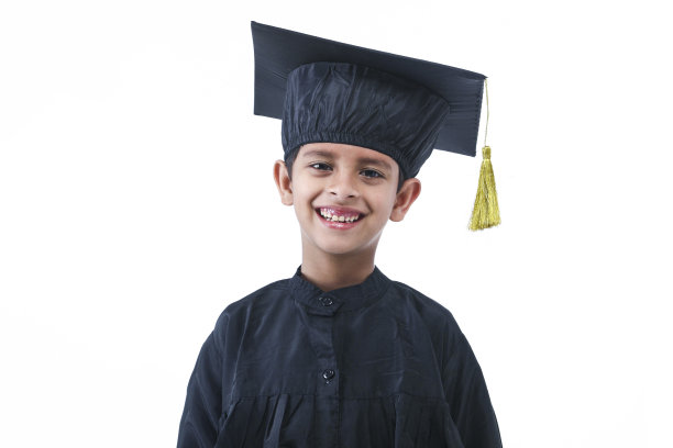 小学男孩戴着毕业帽和毕业服，手拿学位站在那里微笑图片下载