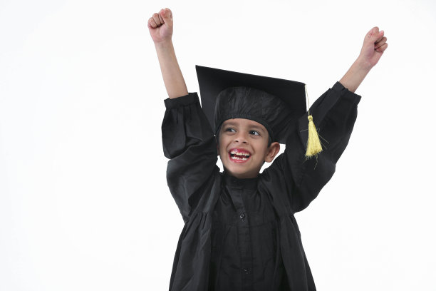 小学男孩戴着毕业帽和毕业服，手拿学位站在那里微笑图片下载