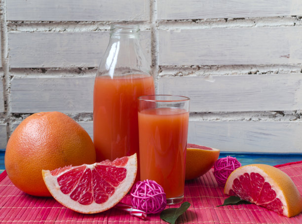 新鲜的葡萄柚汁在一个清晰的高脚杯和玻璃瓶葡萄柚片在一个木制的背景靠近图片下载