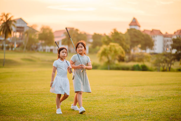 两个亚洲中国微笑的年轻女孩在美丽的日落高尔夫球场有联系的时间图片下载
