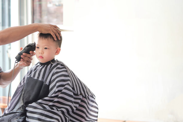 可爱的亚洲小男孩在理发店理发，用发型师的机器剪图片下载