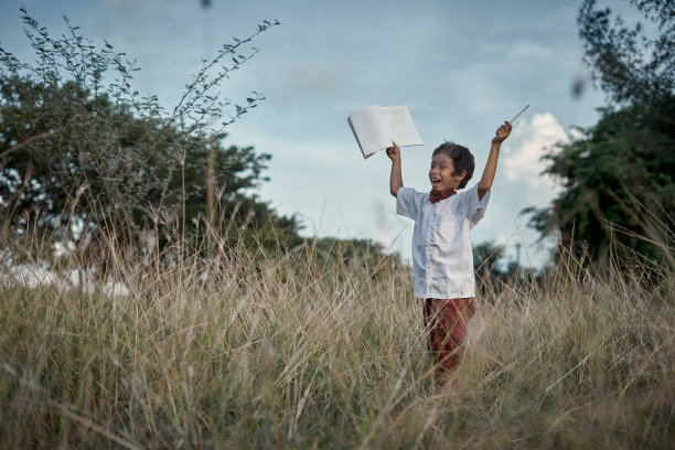 一个穿着校服的男孩站在草地上，手里拿着一本书图片下载