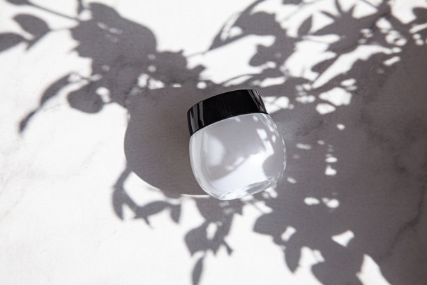 大理石地板上放着一个漂亮的白色奶油罐，在明亮阳光下的树叶阴影中。图片下载