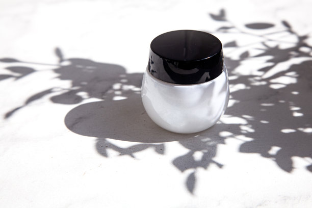 大理石地板上放着一个漂亮的白色奶油罐，在明亮阳光下的树叶阴影中。图片下载