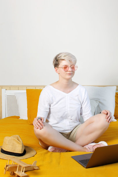 黎明时分，金发漂亮的时髦年轻女子坐在床上，坐在笔记本电脑前，在网上冥想，图片下载