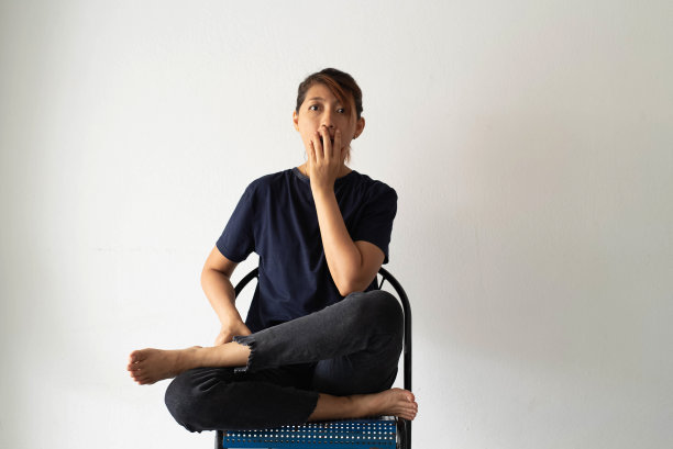 女子靠墙坐着，举起手捂住嘴，睁大眼睛。震惊和害怕的情绪图片下载