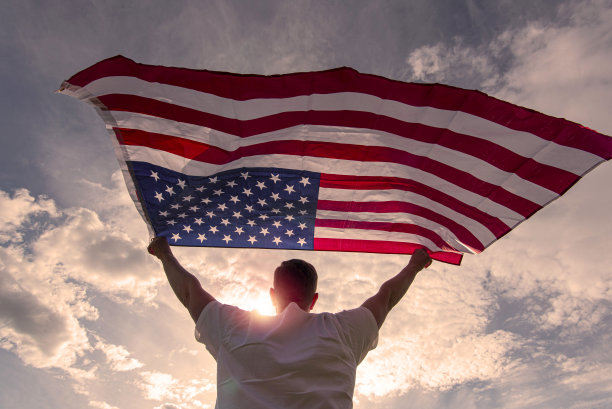 在美国温暖阳光明媚的夜晚，一名男子挥舞着美国国旗，概念图片图片下载