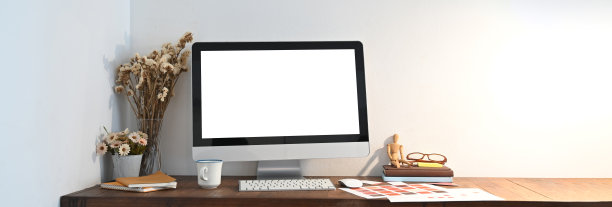 一个木制的工作空间被一个白色的空白屏幕电脑显示器和各种设备包围着。图片下载