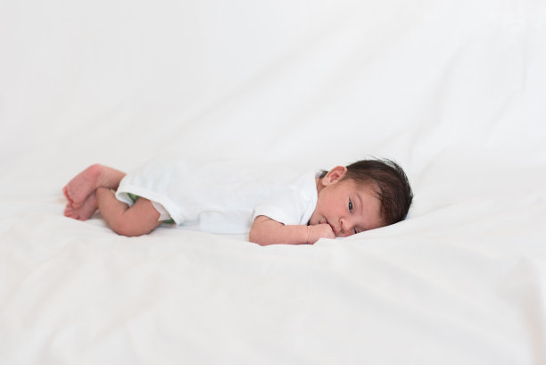 刚出生的男婴躺在床上，用嘴叼着他的手图片下载