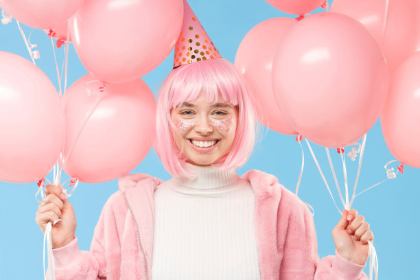 年轻快乐微笑的女孩手里拿着粉红色的气球，享受派对，孤立在蓝色的背景上图片下载