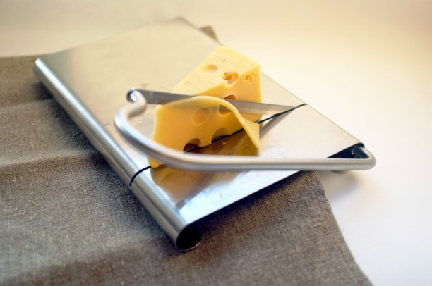 奶酪放在金属奶酪切割器上。带手柄的金属奶酪切片机。在一个工艺纺织桌布的背景，特写。白色背景，水平格式，自然光。图片下载