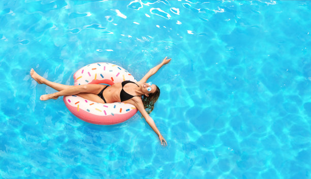 年轻的白人女孩在性感的比基尼漂浮在甜甜圈在游泳池，空的空间图片下载