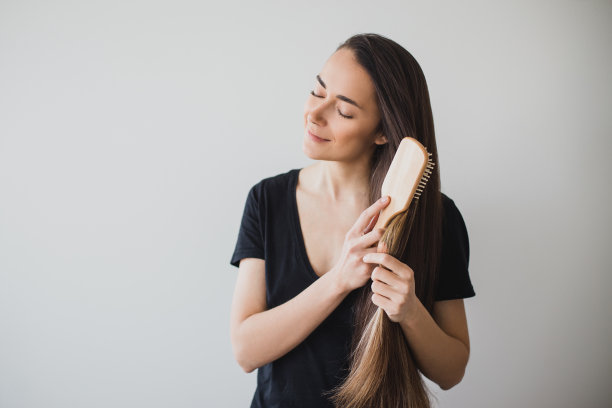 年轻美丽快乐的女子用木质发刷梳理着她健康的长发。图片下载