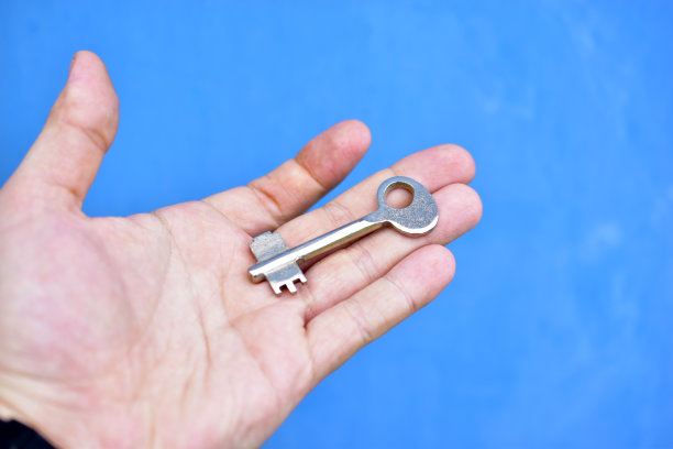 一个蓝色背景的男人手里拿着金属门钥匙图片下载
