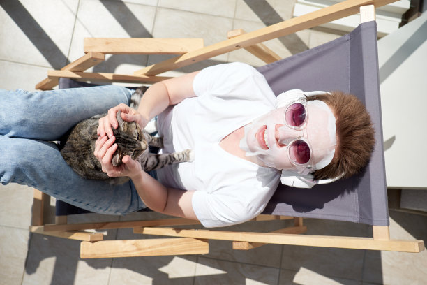 有魅力的女孩，留着时髦的发型，在脸上敷面膜，玩猫，戴着耳机听音乐。图片下载