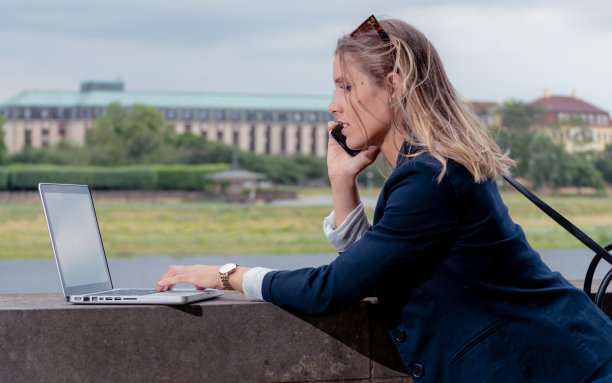 年轻的女商人，在电话中谈论，工作的压力。背景是河流和城市。图片下载