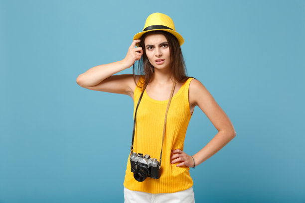 旅行者女游客在黄色夏季休闲衣服帽子与照片相机孤立在蓝色背景。女性悲伤的乘客在周末出国旅行度假航空飞行旅行的概念图片下载