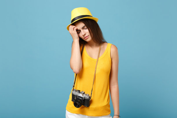 旅行者女游客在黄色夏季休闲衣服帽子与照片相机孤立在蓝色背景。女性悲伤的乘客在周末出国旅行度假航空飞行旅行的概念图片下载