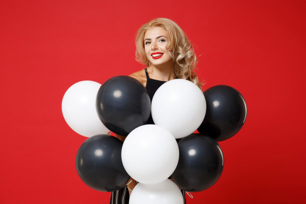微笑的年轻女子女孩在黑色衣服摆孤立在明亮的红色背景在工作室。情人节生日派对的概念。模拟拷贝空间。庆祝，举着气球。图片下载