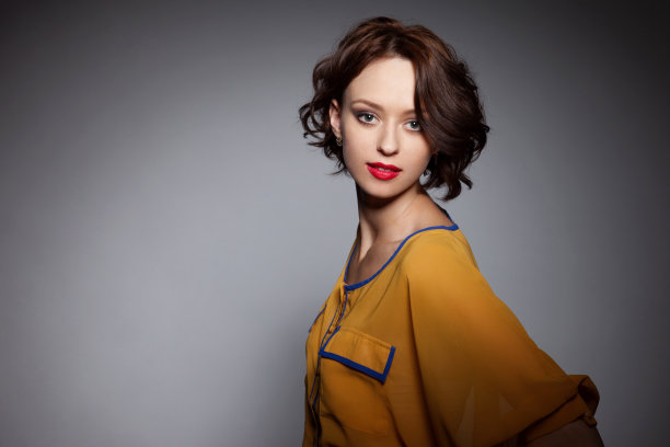 一个年轻的短发女人的正面肖像看着相机，与化妆和红色的嘴唇，在灰色的背景。图片下载