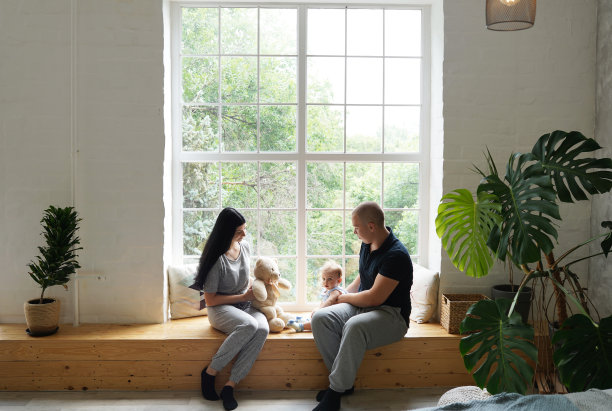 年轻的家庭，父母和小儿子坐在大窗户旁，给孩子看一只泰迪熊图片下载