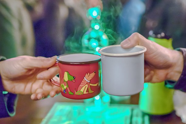 红色和灰色珐琅杯与热饮在男人的手在节日的街道背景图片下载