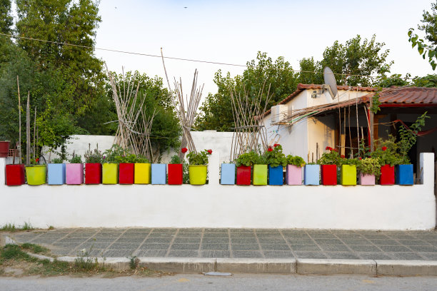 在希腊街道附近的院子里，混凝土白色篱笆上有五颜六色的花盆和鲜花图片下载