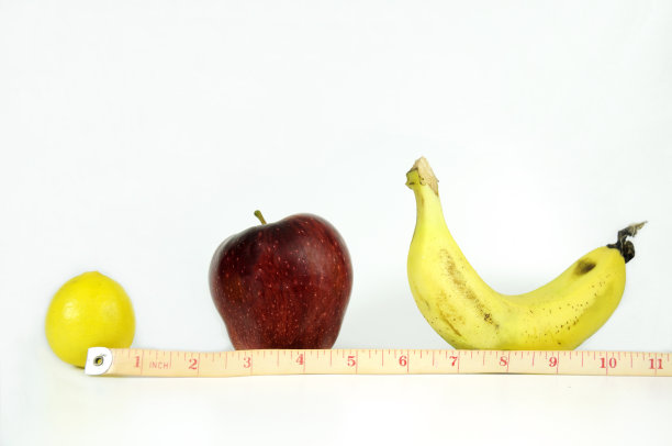 测量尺以英寸为单位将柠檬、苹果、香蕉包裹在白色的表面上，这表明如果你想拥有一个好身材，你需要注意你的饮食。图片下载