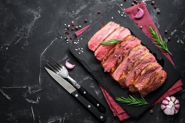 多汁美味的烤牛排，半熟切成块在石板板上，黑色的石头背景。俯视图，平放，复制空间。图片下载