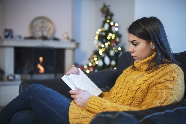 一个年轻女人在圣诞节的壁炉旁看书图片下载