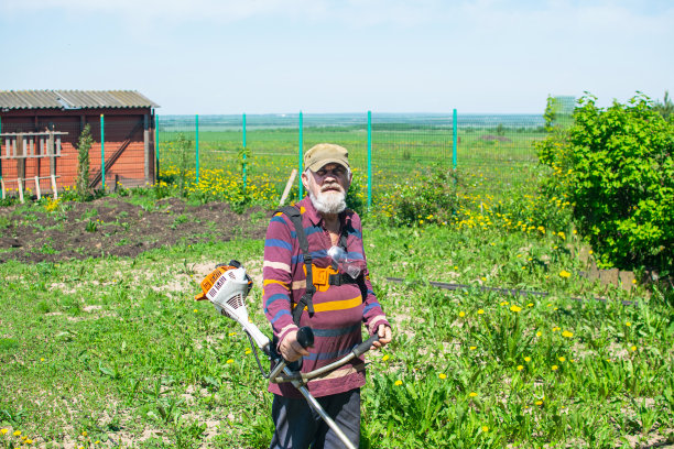 一位老人在他的房子里用电动修剪机割草。图片下载