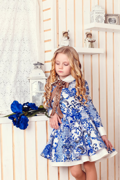 时尚室内照片美丽的孩子。女孩穿着俄罗斯传统的蓝色装饰图案的裙子在木制的背景图片下载