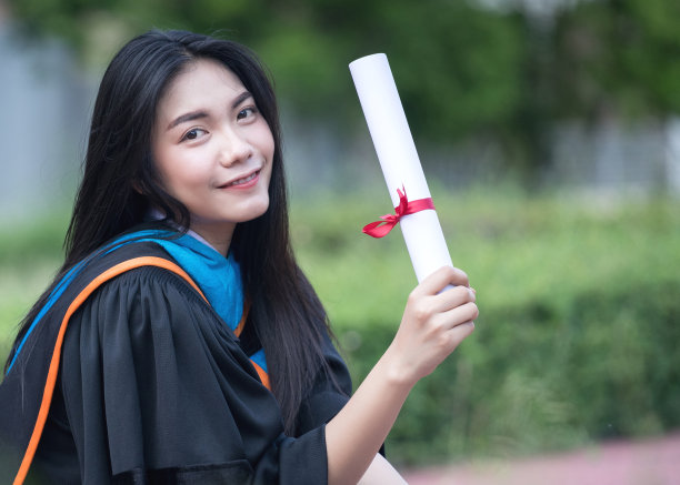 在毕业典礼上，年轻的亚洲女大学毕业生穿着毕业礼服和帽子在大学校园里庆祝学位。教育库存图片。图片下载