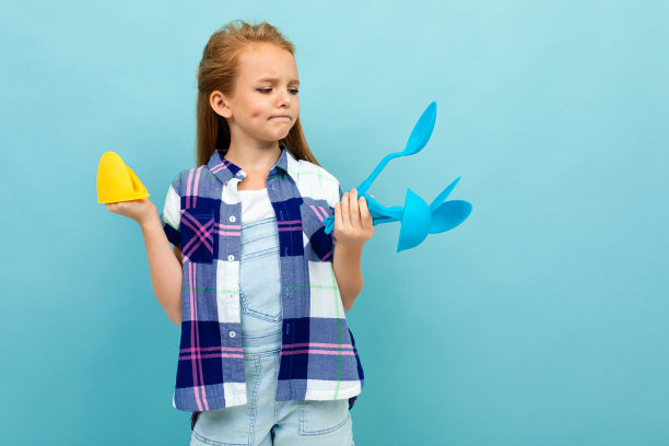 一个沉思的欧洲女孩，手里拿着烤箱手套和餐具，站在浅蓝色的墙上图片下载