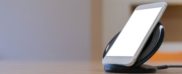近距离的智能手机侧视图与隔离模拟屏幕充电电池电压的无线充电器设备在办公桌上的技术生活方式的概念图片下载
