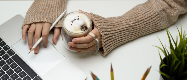 女性拿着笔记本电脑，在白色的工作台上端着一杯饮料图片下载