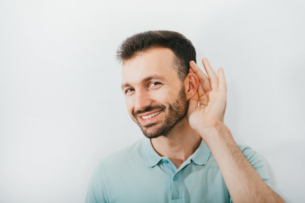 检查你的听力。一个乐观的男人在灰色的背景下，用手靠近他的耳朵。听力的健康、治疗和诊断图片下载