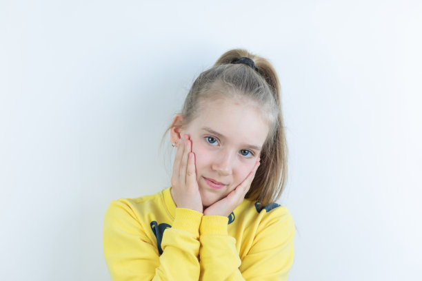 生动或色彩丰富的工件与搞笑，酷，漂亮和漂亮的女孩在黄色毛衣或t恤在白色的背景容易提取失望或遗憾的姿势，鬼脸与手掌在脸颊图片下载