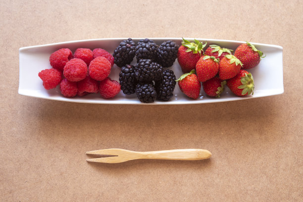 森林水果，覆盆子，黑莓和草莓放在一个长方形的盘子里，底部是棕色的，有阴影，在照片上可以写文字的区域。图片下载