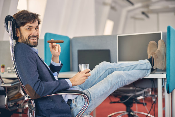 一个在工作中抽着雪茄喝着苏格兰威士忌的快乐的年轻人图片下载