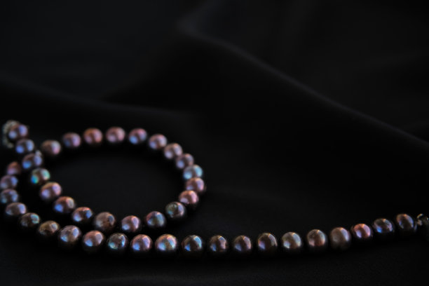 优雅的黑色丝绸背景与紫色珍珠项链。图片下载