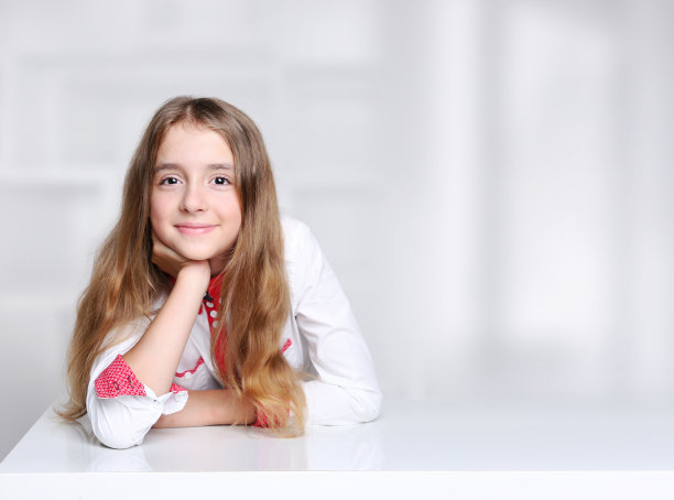 小女孩坐在空桌子旁。小学生肖像产品推广设计。穿着白衬衫的小学生。图片下载