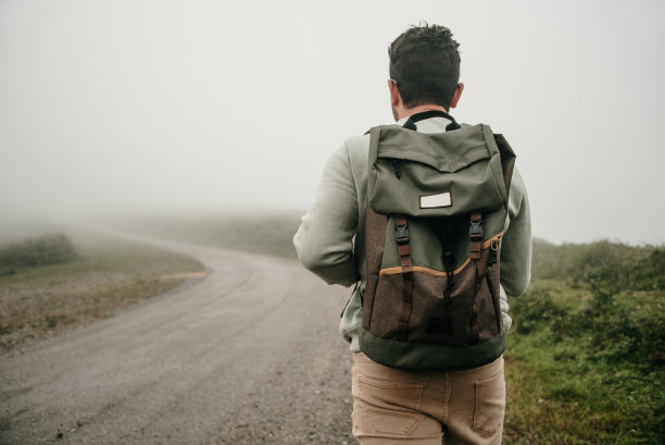 后视图的男人与背包走在一个雾蒙蒙的道路上图片下载