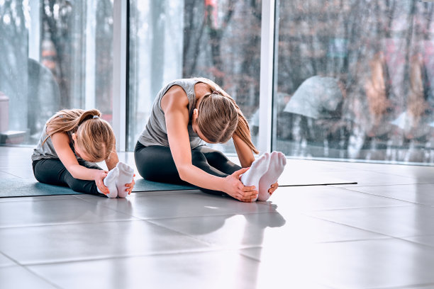 运动的母亲和女儿。快乐的母女坐在运动俱乐部的运动垫上做伸展运动，面带微笑图片下载