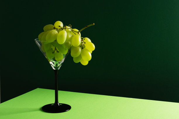 一串新鲜成熟的白葡萄放在桌上的玻璃杯里。图片下载