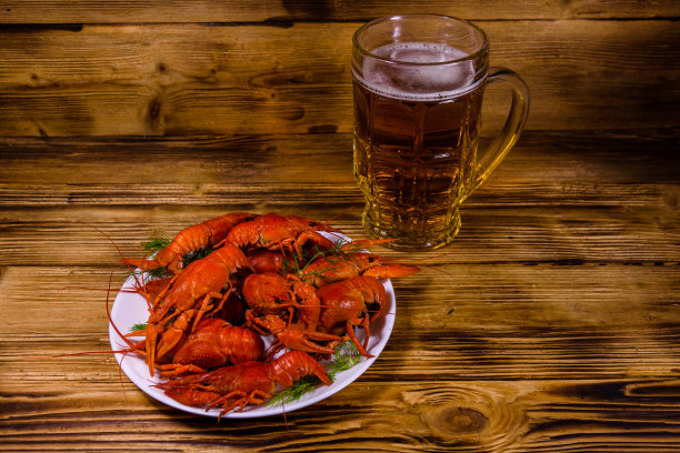 木桌上放着一杯啤酒和煮小龙虾图片下载