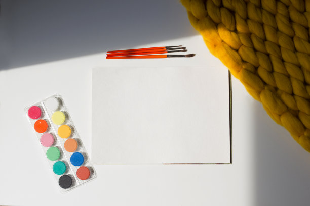 美术设备:空白纸，颜料，画笔和调色板上的白色和黄色毯子背景图片下载