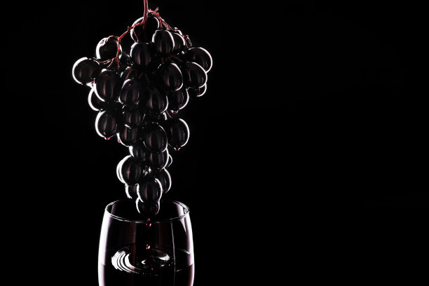 葡萄滴酒入酒杯。红酒倒入酒杯。孤立在黑色背景上。图片下载